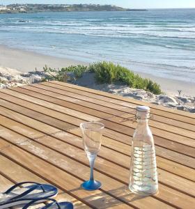 a bottle and a wine glass sitting on a table near the beach at Rooisee in Yzerfontein