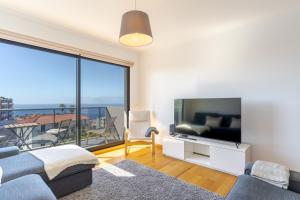 een woonkamer met een tv en een groot raam bij Jardins do Oceano in Caniço