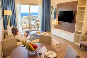 a woman sitting on a couch reading a book in a living room at Helnan Mamoura Hotel & Events Center in Alexandria