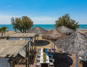 a table with chairs and straw umbrellas on a beach at Pareus Beach Resort in Caorle
