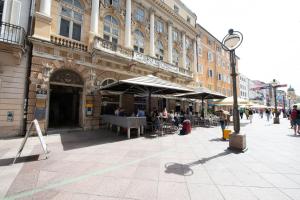 a building with people sitting under umbrellas on a street at Apartment Korzo Filodrammatica in Rijeka