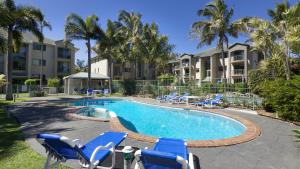 a swimming pool with blue chairs and palm trees at Pacific Place Apartments in Gold Coast