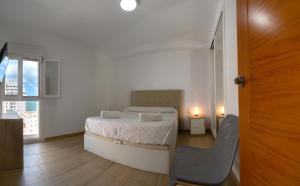 biała sypialnia z łóżkiem i krzesłem w obiekcie Zurbarán Playa Ha Apartment w Kadyksie
