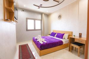 um quarto com uma cama com lençóis roxos e uma janela em HOTEL BEAUPORT em Laayoune