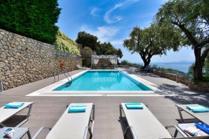 uma piscina com cadeiras brancas e uma parede de pedra em Athiri House Villa Corfu em Spartýlas