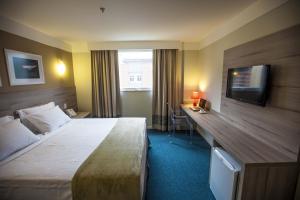 a hotel room with a bed and a desk and a television at Intercity Teresópolis in Teresópolis