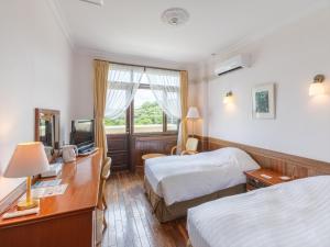 a hotel room with two beds and a desk and a television at Ada Garden Hotel Okinawa in Kunigami