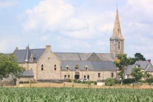 an old stone church with a steeple and a field at le coin des hirondelles in Pontorson