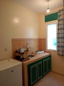 eine Küche mit grünen Schränken, einem Waschbecken und einem Fenster in der Unterkunft Dar Bouanani in Asilah