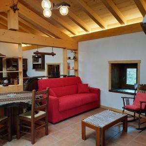 a living room with a red couch and a kitchen at La Casa nel Bosco - Your Mountain Holiday in Casargo