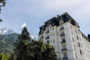 ein hohes weißes Gebäude mit Bergen im Hintergrund in der Unterkunft Le Majestic 145 Appt - Chamonix All Year in Chamonix-Mont-Blanc