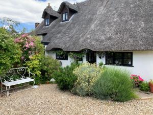 伍爾的住宿－The Cottage Studio，白色的房子,有茅草屋顶和长凳