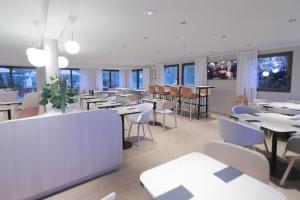 un restaurant avec des tables blanches, des chaises et des fenêtres dans l'établissement Hôtel Antares & Spa, à Honfleur