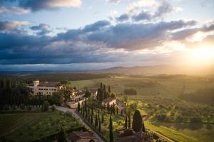 a view of a villa in a field with the sun setting at COMO Castello Del Nero in Tavarnelle in Val di Pesa