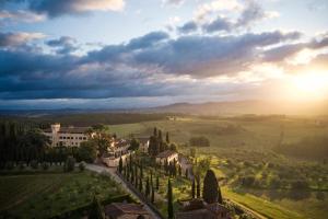 una vista de una villa en un campo con puesta de sol en COMO Castello Del Nero en Tavarnelle in Val di Pesa