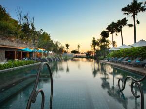 a swimming pool at a resort with chairs and palm trees at Hotel Indigo Bali Seminyak Beach by IHG in Seminyak