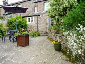 eine Terrasse mit einem Tisch, einem Sonnenschirm und Blumen in der Unterkunft Cloudberry Cottage in Stanton in Peak