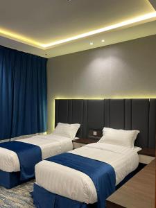 two beds in a hotel room with blue curtains at قمم بارك Qimam Park Hotel 2 in Abha