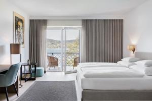 a hotel room with two beds and a desk and a balcony at Hotel Linde 4 S in Maria Wörth