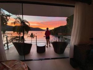 un homme debout sur un balcon donnant sur le coucher du soleil dans l'établissement Asalem, à Abraão