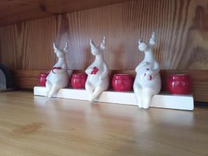 tre conigli bianchi seduti su un tavolo con tazze rosse di Casa Ciclamino a Serrada