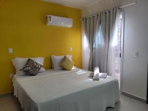 - une chambre avec un grand lit blanc et un mur jaune dans l'établissement Apartamentos da Gaby, à Morro de São Paulo