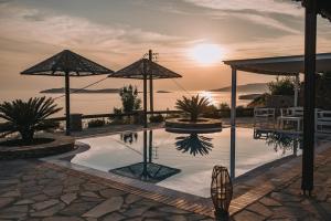 a pool with umbrellas and a sunset in the background at Blue Bay Resort Village in Batsi