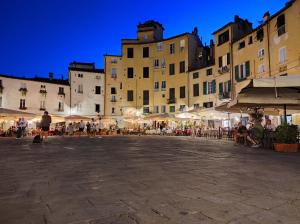 un grupo de personas sentadas en mesas en una plaza con edificios en Casina di Tea Lucca, en Lucca