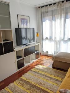 una sala de estar con TV en un centro de entretenimiento blanco en Iradri, Apartamento Playa Gijón, en Gijón