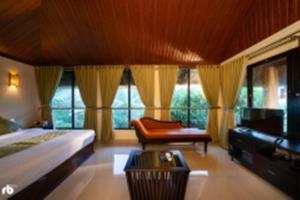 a bedroom with a bed and a chair and windows at Kuruva Isles Jungle Resort in Wayanad