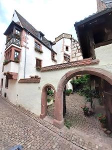 un gran edificio blanco con un arco en una calle en ADRIHOF à Riquewihr, Cour de l'Abbaye d'Autrey en Riquewihr