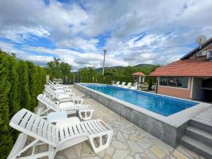 a row of white lounge chairs next to a swimming pool at Djokić 2 sa bazenom in Soko Banja