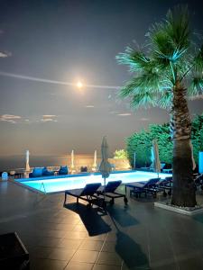a pool with chairs and a palm tree at night at Golden View Residence in Dhërmi
