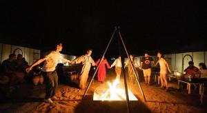 a group of people standing around a fire at night at Camp Sahara berber in Merzouga