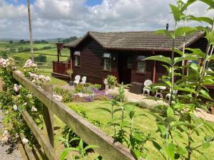 a small wooden house with a fence and flowers at The Nest in Modbury