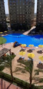 a large swimming pool with yellow umbrellas and palm trees at Studio apartment, Aqua View Resort, North coast in El Alamein