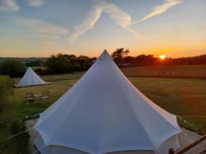 a white tent in a field with the sunset at Tryfan Pen Cefn Farm Bell Tent in Abergele