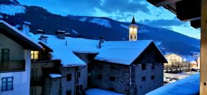 eine schneebedeckte Stadt mit einem Uhrturm im Hintergrund in der Unterkunft Trilocale mansardato nel cuore della Val Di Fiemme in Ziano di Fiemme