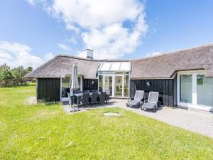 a house with a patio with chairs and an umbrella at Holiday home Vejers Strand XX in Vejers Strand