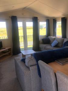 a living room with couches and a table and windows at Gwel y Môr - Lleyn Peninsula Static in Llangwnadl