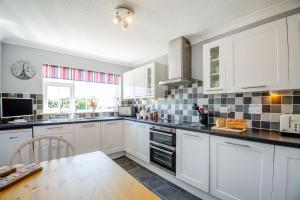 a kitchen with white cabinets and a table and a window at Cororion Cottage in Benllech