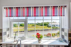a kitchen window with a colorful striped curtain at Cororion Cottage in Benllech +14 photos