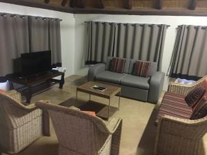 een woonkamer met een bank, een tv en stoelen bij River Hill Lodge in Komatipoort