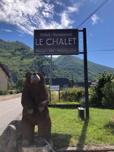 ein großer brauner Teddybär sitzt neben einem Straßenschild in der Unterkunft Hotel Le Chalet in Sainte-Marie-de-Campan
