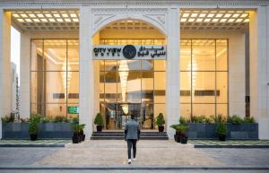 Un uomo che cammina davanti a un palazzo di City View Hotel- Managed by Arabian Link International a Kuwait