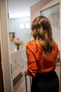 Eine Frau in einem orangenen Hemd, die in einen Spiegel schaut. in der Unterkunft Palazzo Bellocchi - Suites & Apartments in Brindisi