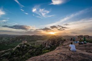 a person sitting on top of a mountain watching the sunset at Vicky's Home Stay Hampi in Hampi