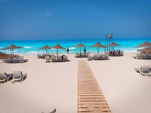 einen Holzweg am Strand mit Stühlen und Sonnenschirmen in der Unterkunft شاليه راقي بمارسيليا بيتش 1 الساحل in Dawwār Muḩammad Abū Shunaynah