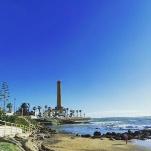 a lighthouse on the beach with palm trees and the ocean at Rompeolas Playa in Chipiona