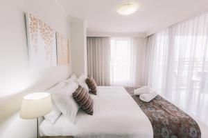 a white bedroom with a large bed and a lamp at Newcastle Central Plaza Apartment Hotel Official in Newcastle